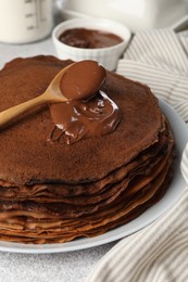 Photo of Delicious chocolate crepes with sweet paste on light grey table, closeup