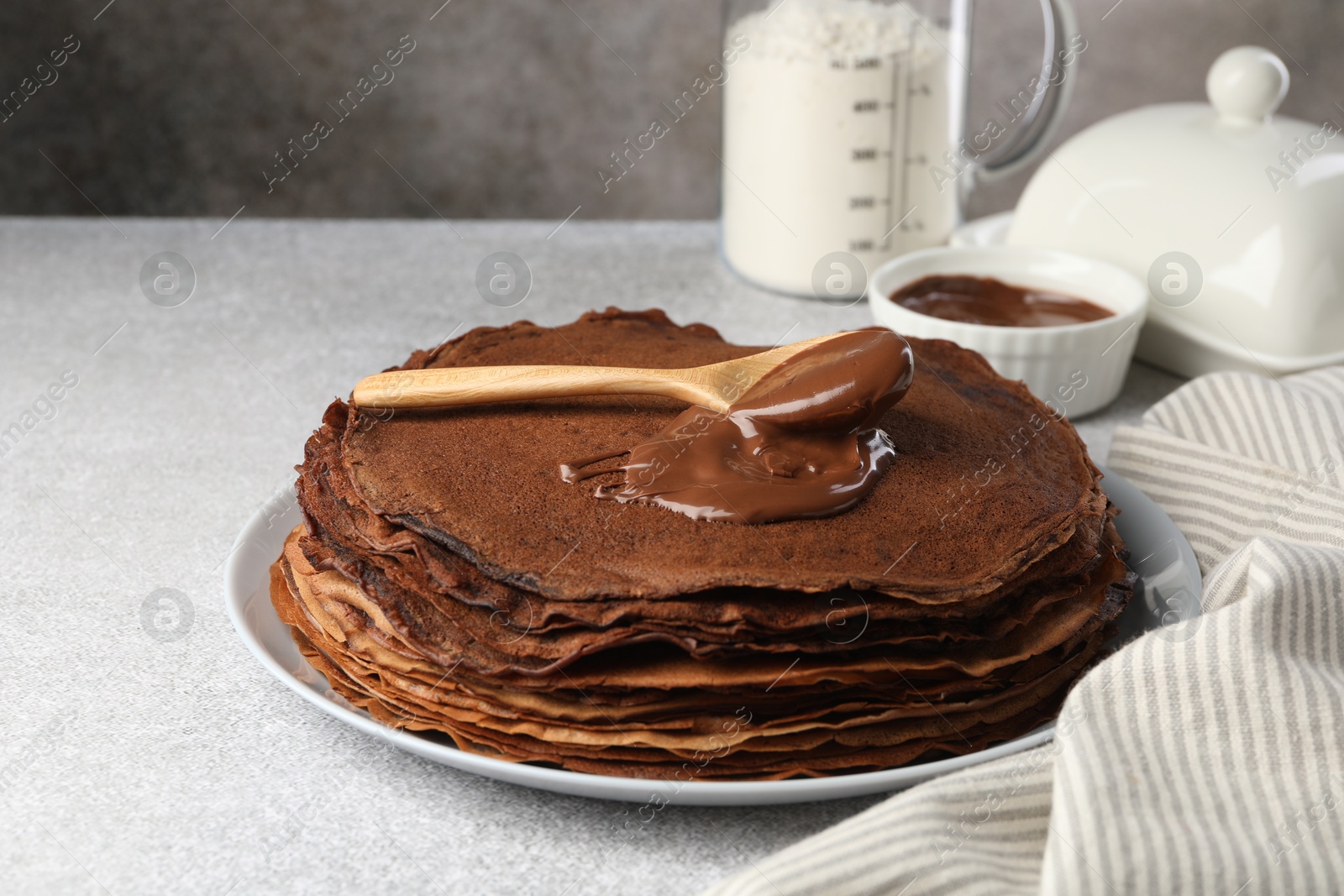 Photo of Delicious chocolate crepes with sweet paste on light grey table, closeup