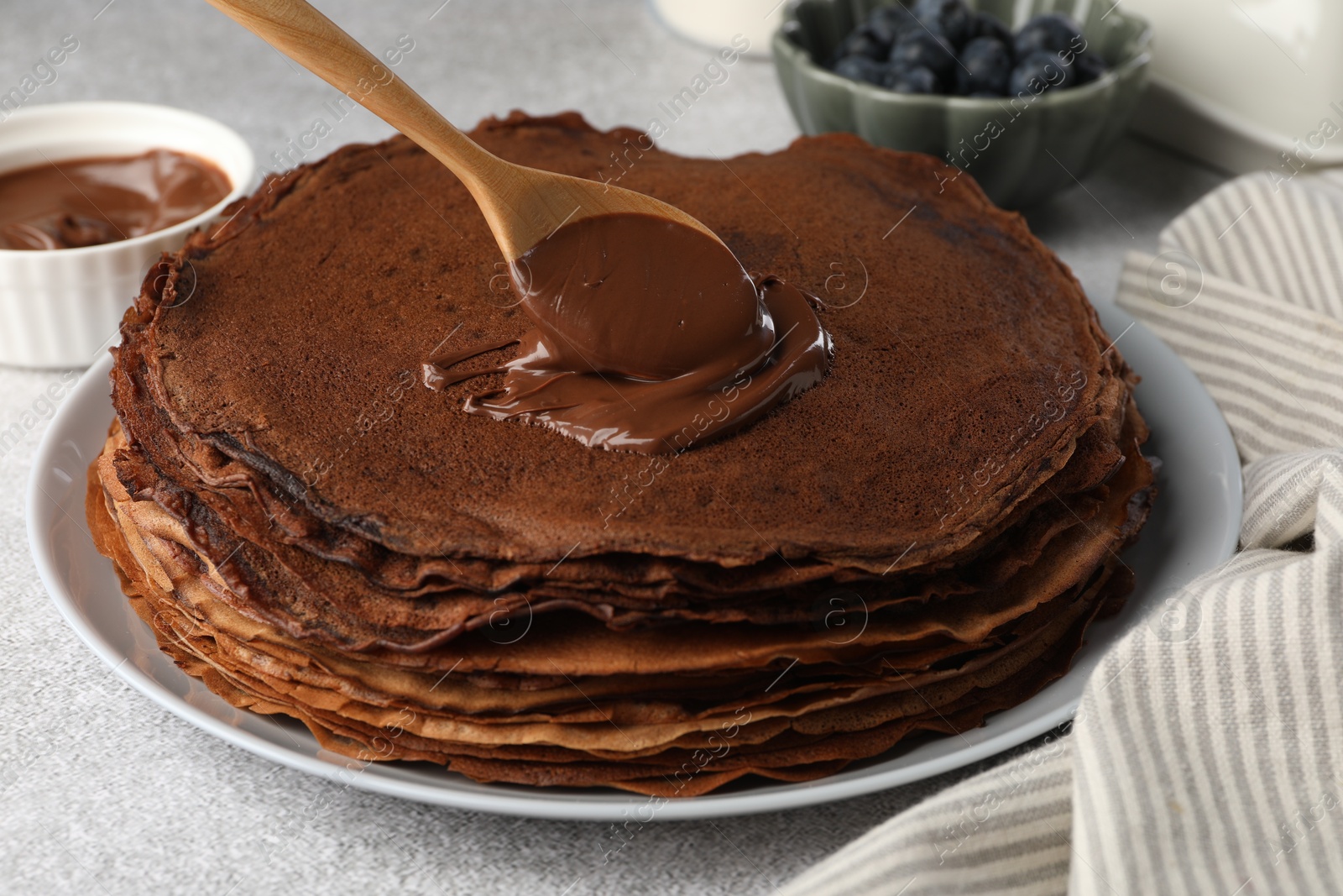 Photo of Delicious chocolate crepes with sweet paste on light grey table, closeup