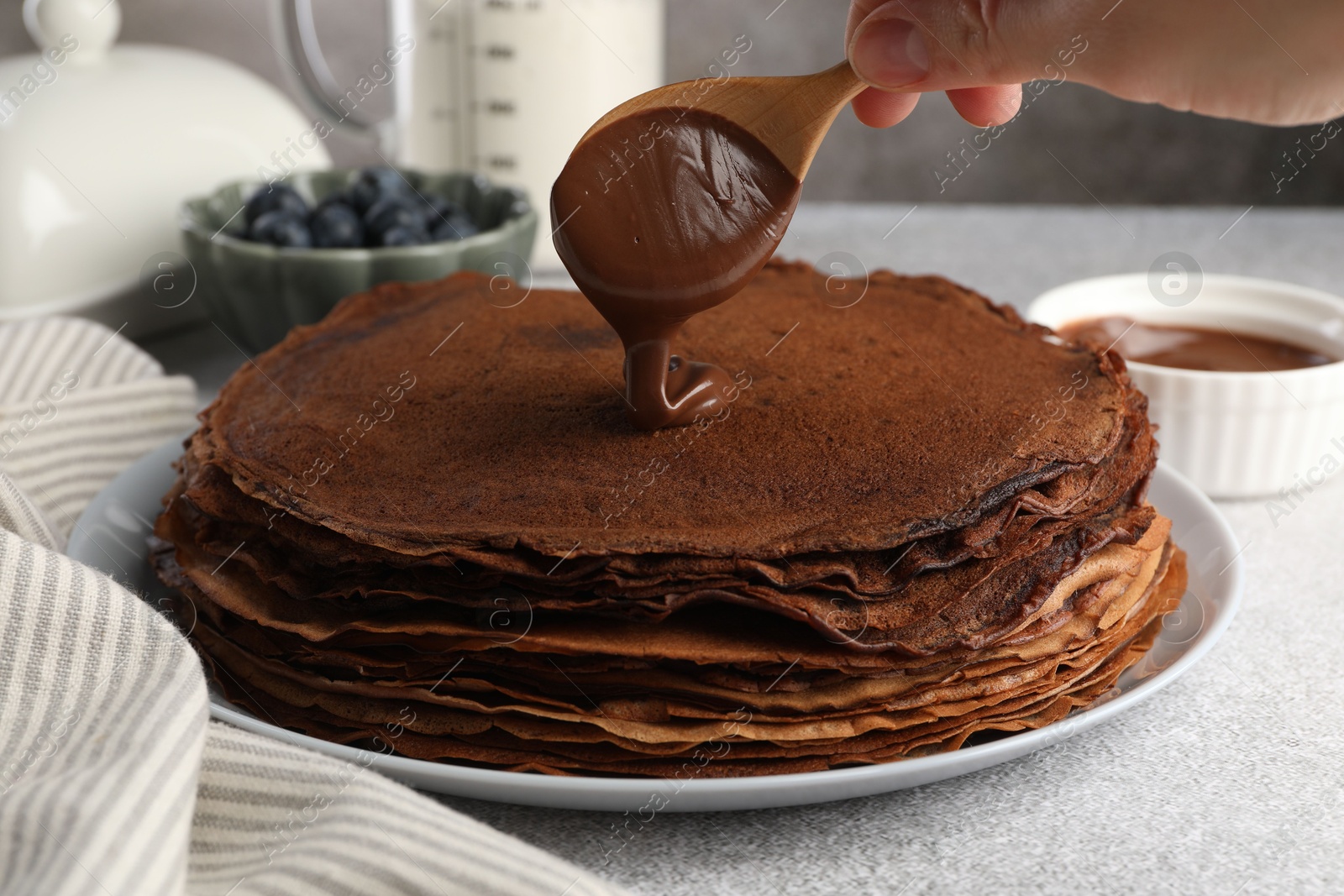 Photo of Woman pouring sweet paste onto delicious chocolate crepes at light grey table, closeup