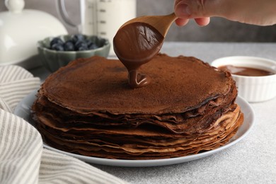 Photo of Woman pouring sweet paste onto delicious chocolate crepes at light grey table, closeup