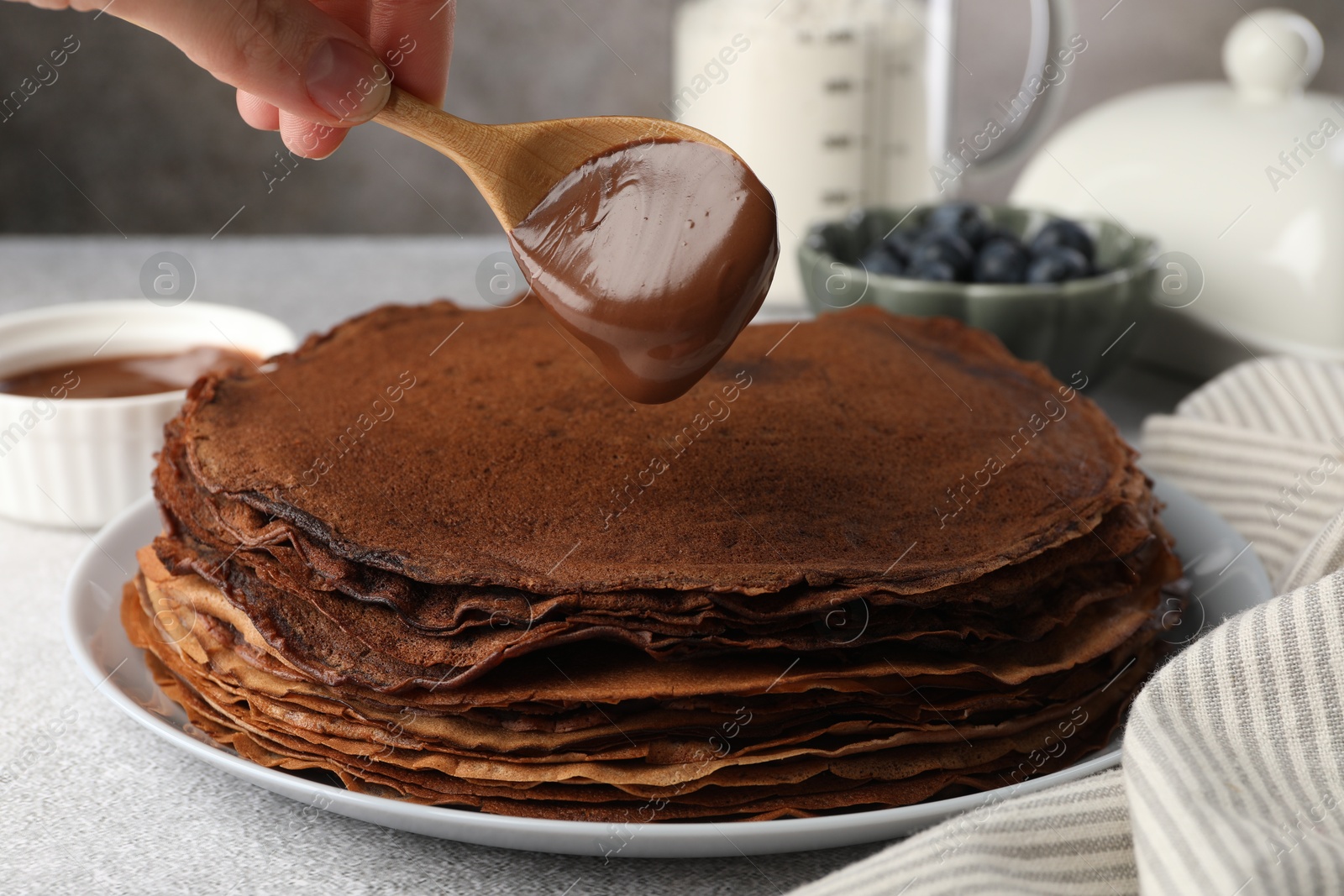 Photo of Woman pouring sweet paste onto delicious chocolate crepes at light grey table, closeup