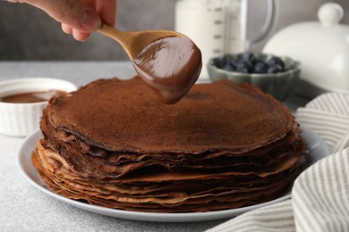 Photo of Woman pouring sweet paste onto delicious chocolate crepes at light grey table, closeup