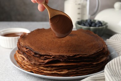 Photo of Woman pouring sweet paste onto delicious chocolate crepes at light grey table, closeup