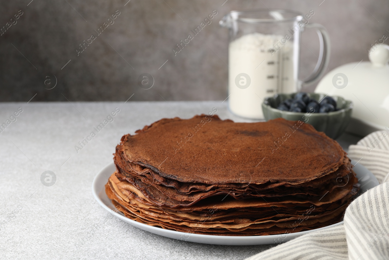 Photo of Delicious chocolate crepes with blueberries on light grey table, closeup