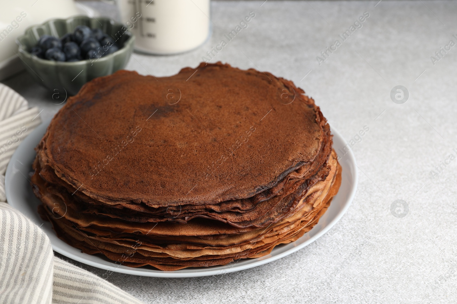 Photo of Delicious chocolate crepes with blueberries on light grey table, closeup