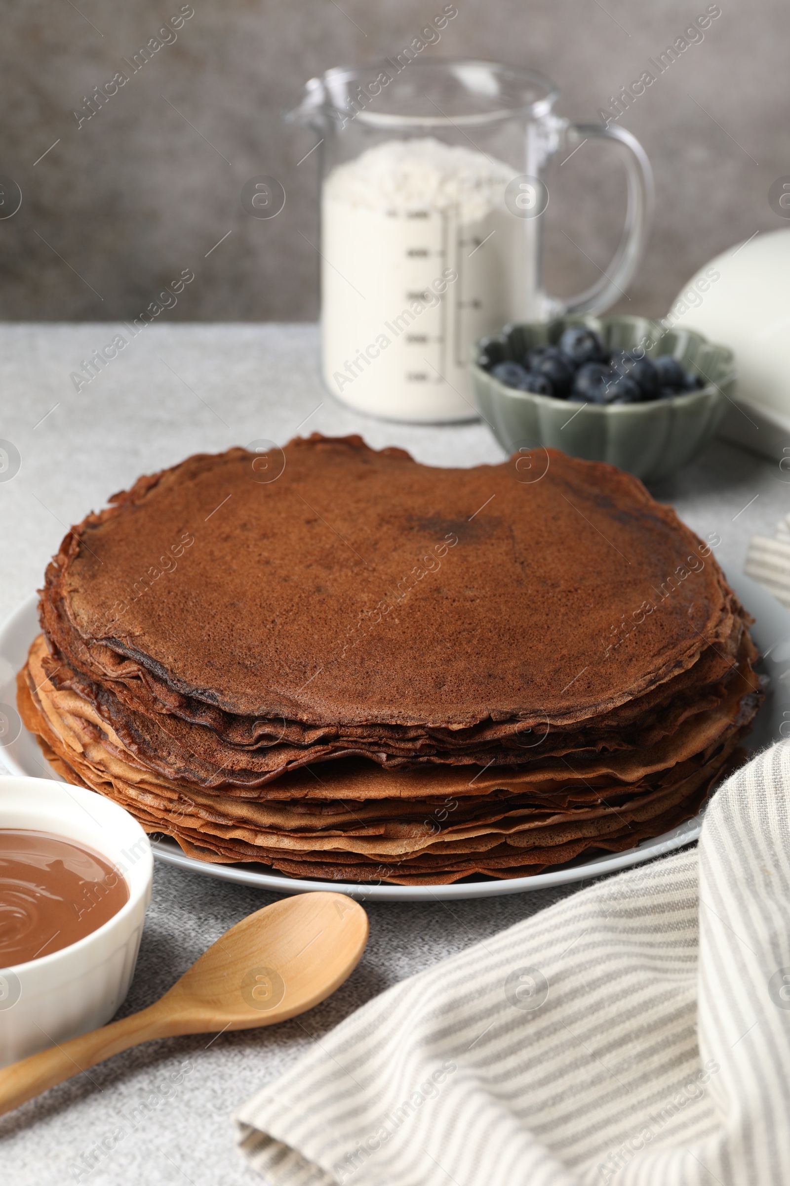 Photo of Delicious chocolate crepes with sweet paste and blueberries on light grey table, closeup