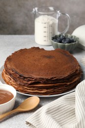 Photo of Delicious chocolate crepes with sweet paste and blueberries on light grey table, closeup