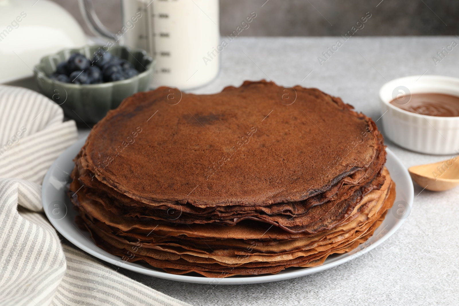 Photo of Delicious chocolate crepes with sweet paste and blueberries on light grey table, closeup