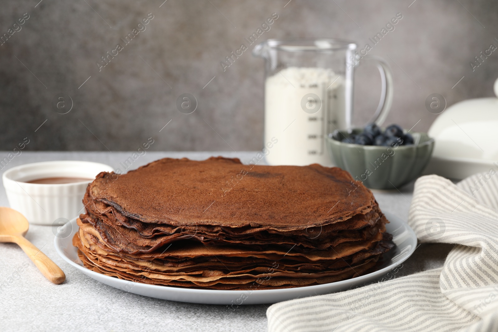 Photo of Delicious chocolate crepes with sweet paste and blueberries on light grey table, closeup