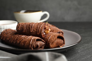 Photo of Delicious chocolate crepes with sweet paste and nuts on black table, closeup