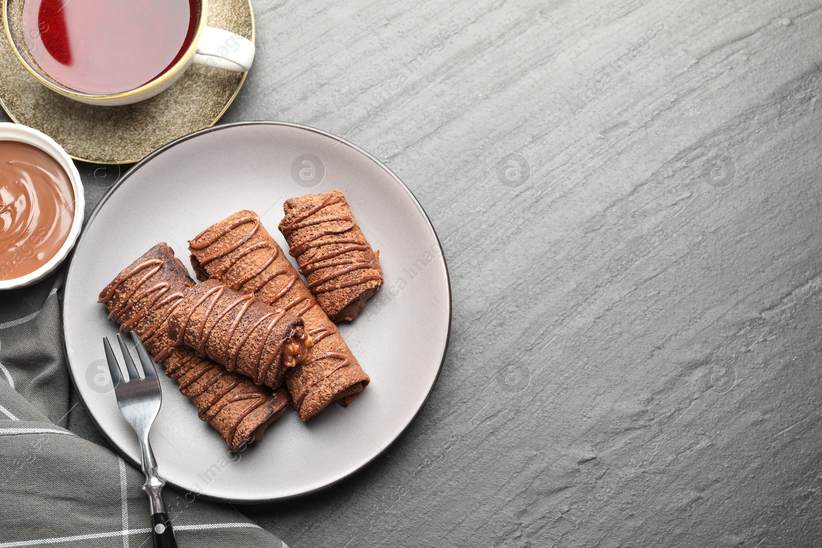 Photo of Delicious chocolate crepes with sweet paste, nuts and tea on black table, flat lay. Space for text