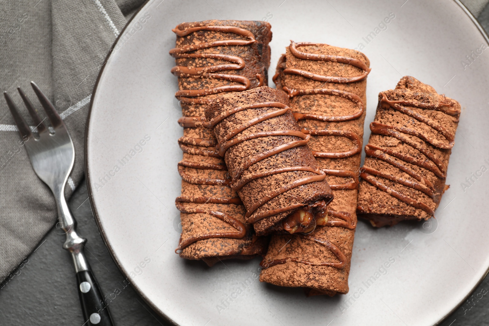 Photo of Delicious chocolate crepes with sweet paste and nuts on black table, top view