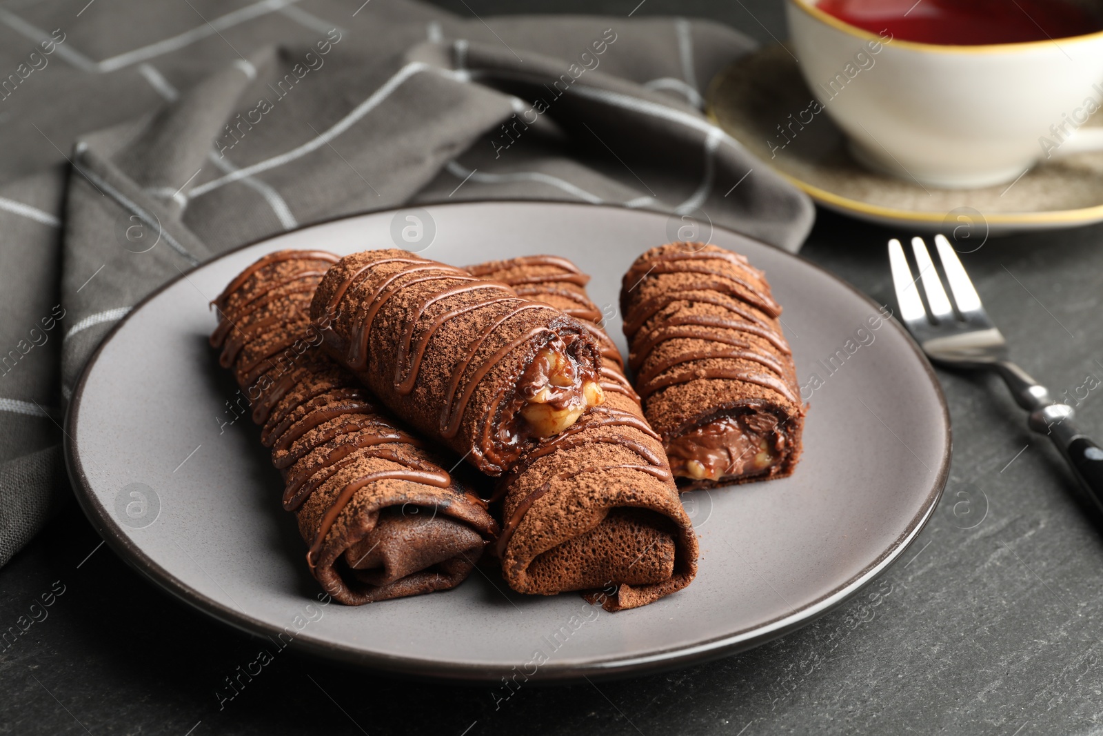 Photo of Delicious chocolate crepes with sweet paste and nuts on black table, closeup