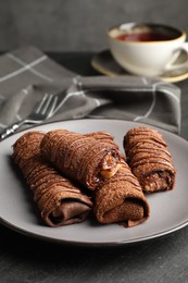 Photo of Delicious chocolate crepes with sweet paste and nuts on black table, closeup