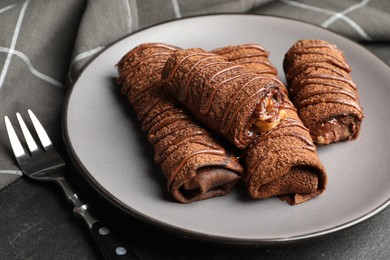 Photo of Delicious chocolate crepes with sweet paste and nuts on black table, closeup