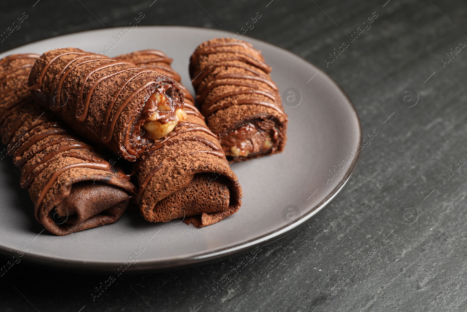 Photo of Delicious chocolate crepes with sweet paste and nuts on black table, closeup