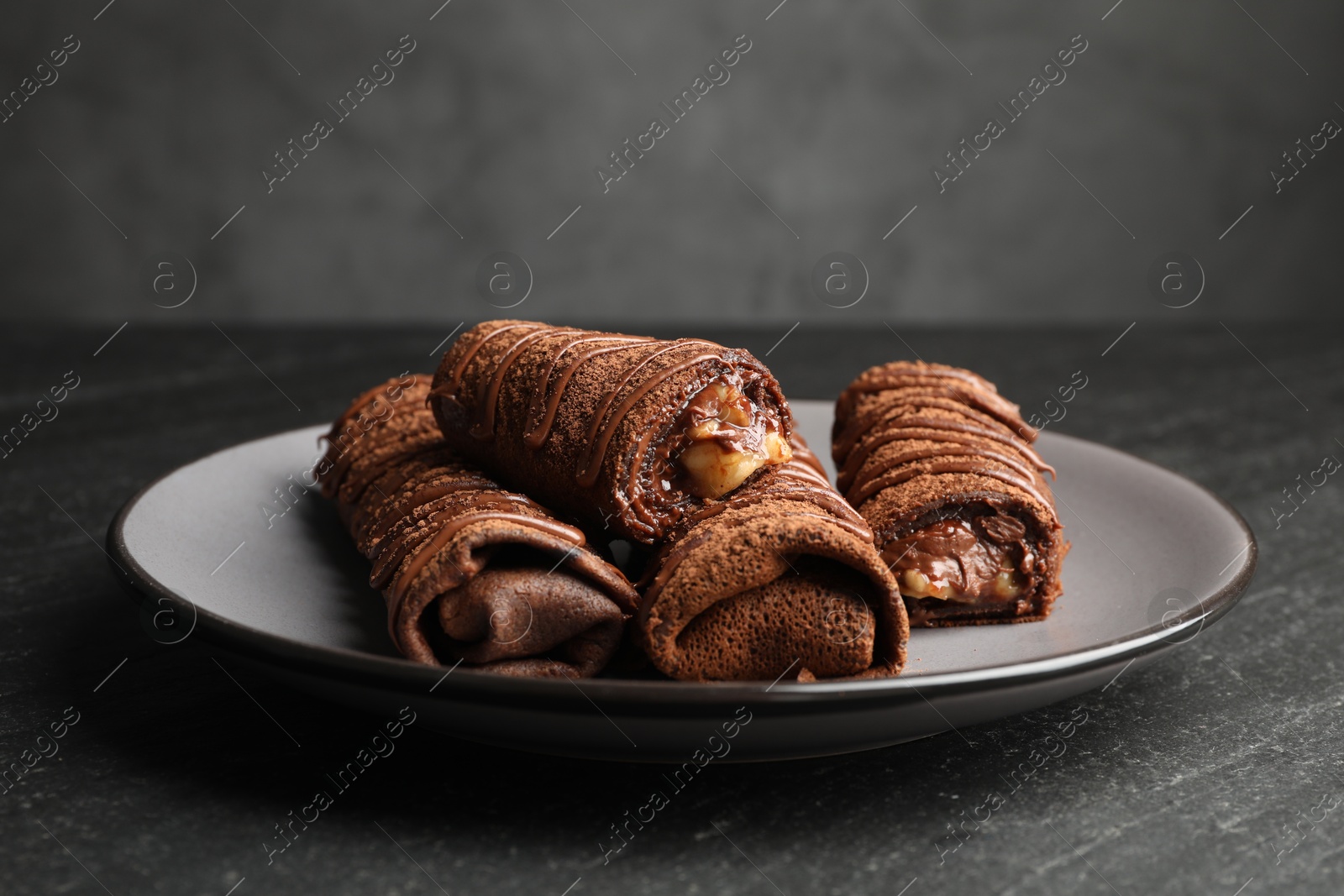 Photo of Delicious chocolate crepes with sweet paste and nuts on black table, closeup