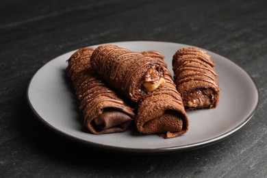 Photo of Delicious chocolate crepes with sweet paste and nuts on black table, closeup