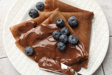 Photo of Delicious chocolate crepes with sweet paste and blueberries on table, top view