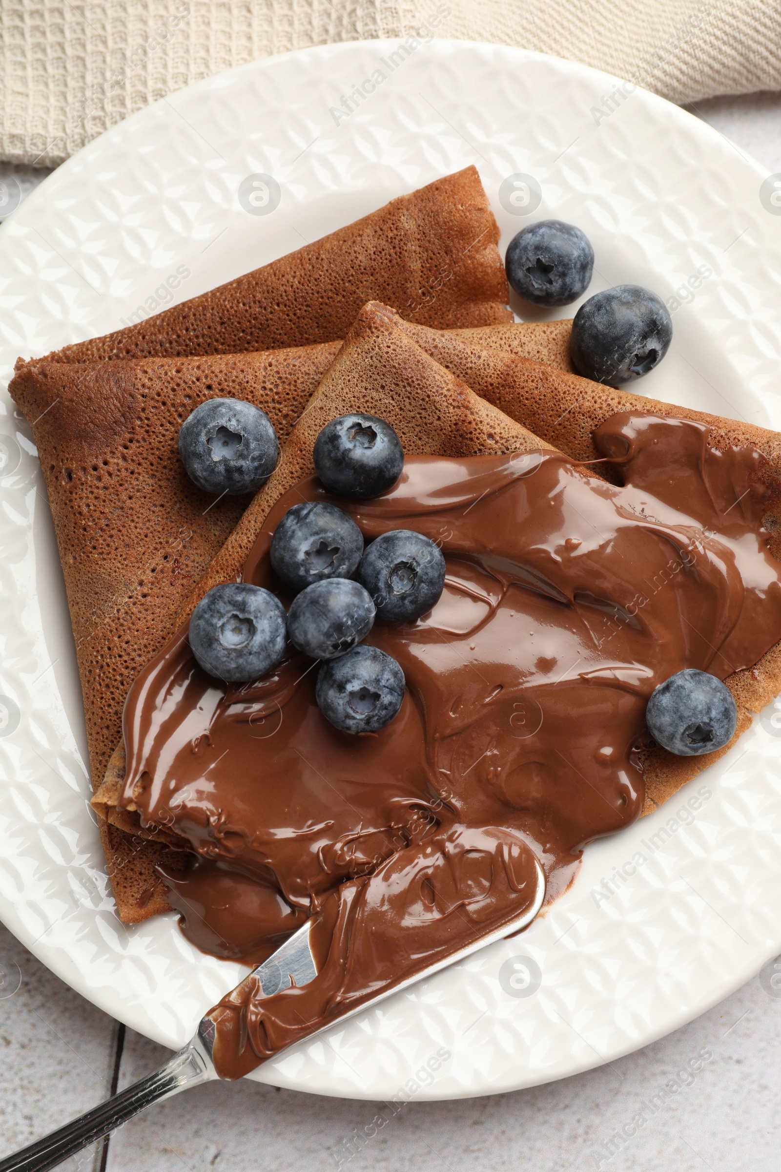 Photo of Delicious chocolate crepes with sweet paste and blueberries on table, top view