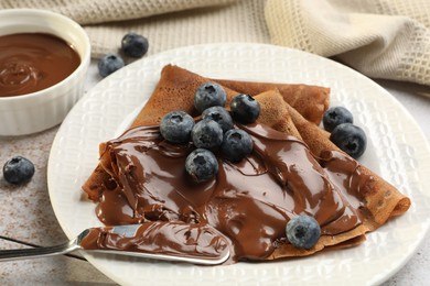 Photo of Delicious chocolate crepes with sweet paste and blueberries on table, closeup