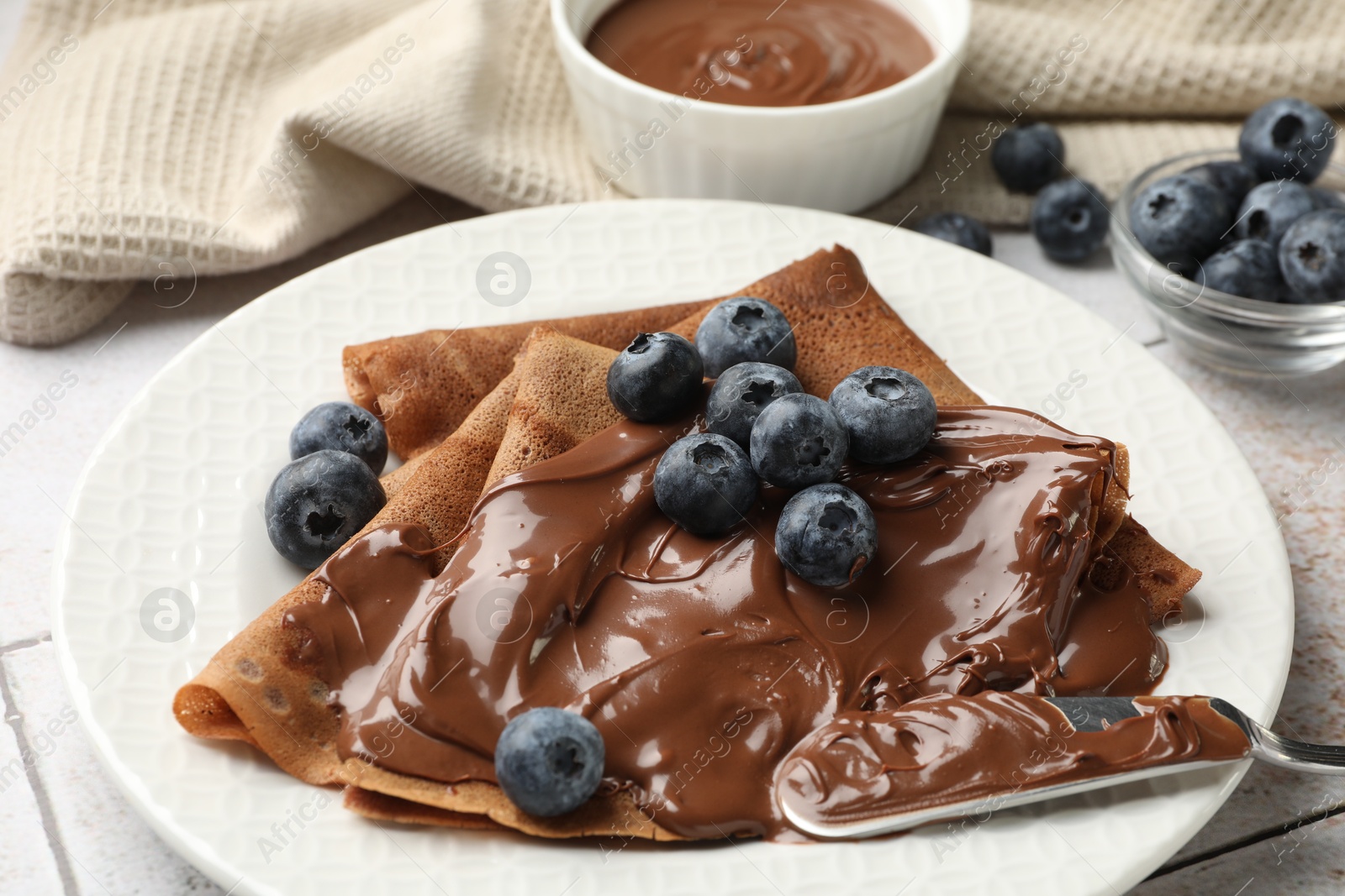 Photo of Delicious chocolate crepes with sweet paste and blueberries on table, closeup