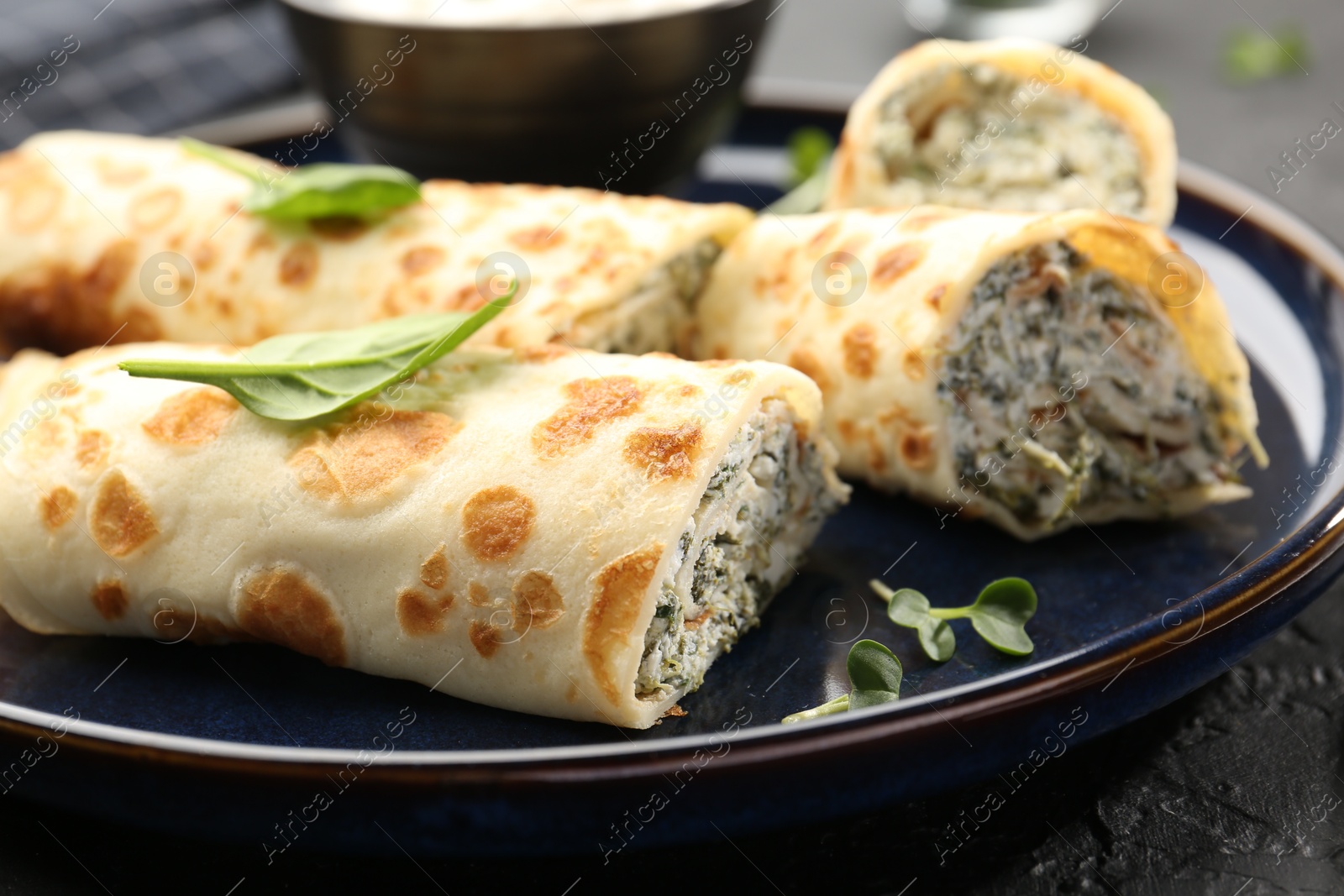 Photo of Delicious crepes with cottage cheese and spinach on black table, closeup