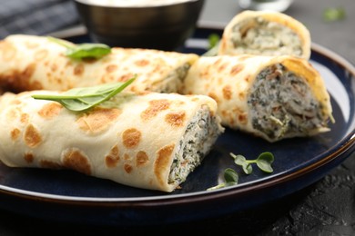 Photo of Delicious crepes with cottage cheese and spinach on black table, closeup