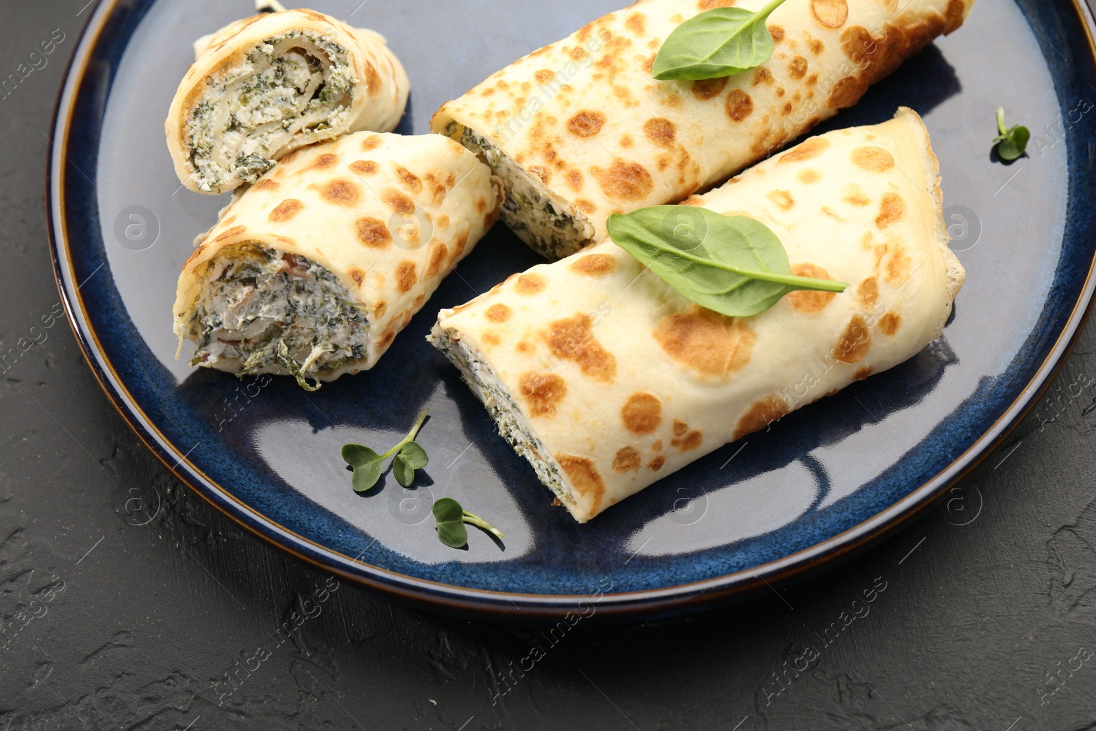 Photo of Delicious crepes with cottage cheese and spinach on black table, closeup