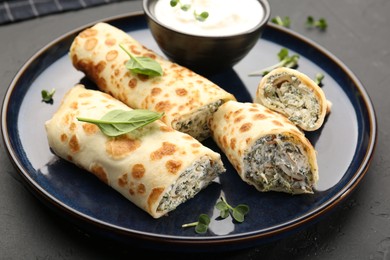 Photo of Delicious crepes with cottage cheese, spinach and sour cream on black table, closeup