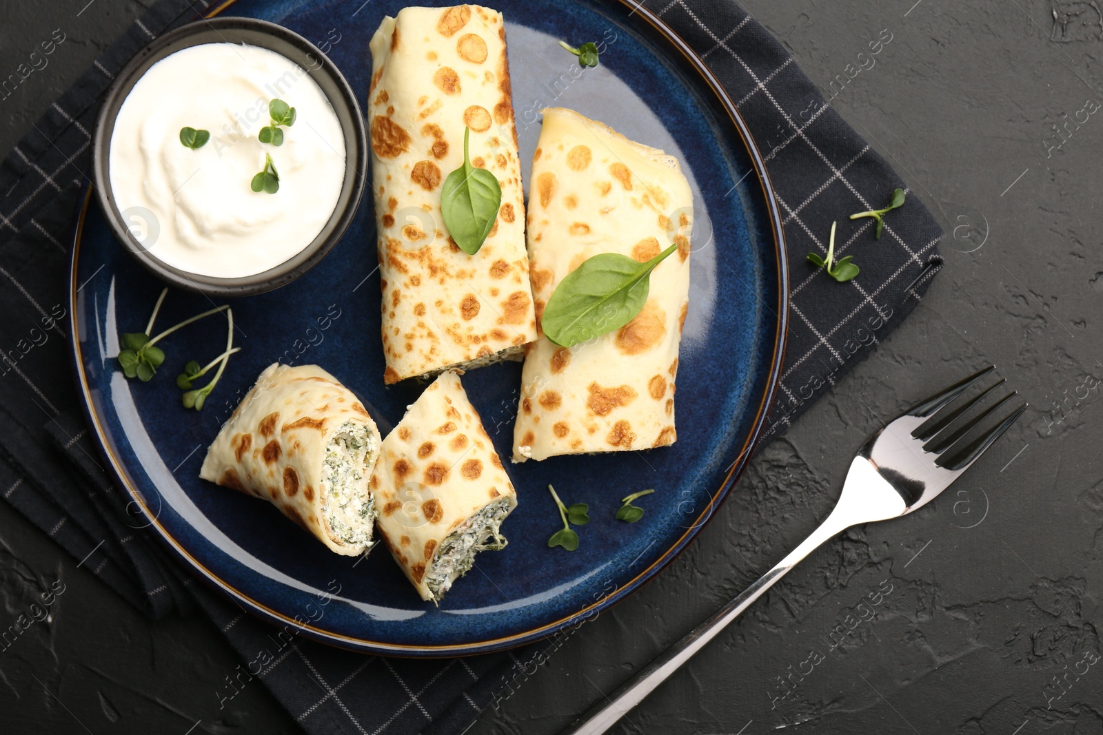 Photo of Delicious crepes with cottage cheese, spinach and sour cream served on black table, top view