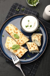 Photo of Delicious crepes with cottage cheese, spinach and sour cream served on black table, top view