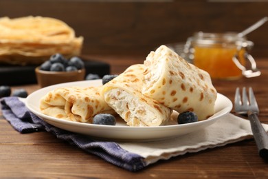 Photo of Delicious crepes with cottage cheese, jam and blueberries served on wooden table, closeup