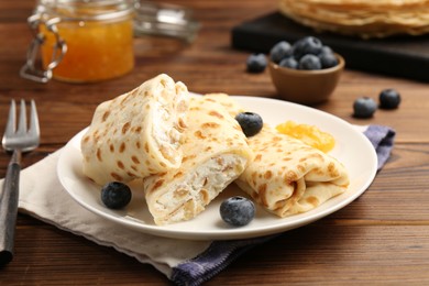 Photo of Delicious crepes with cottage cheese, jam and blueberries served on wooden table, closeup