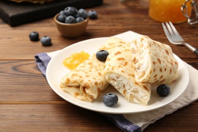 Photo of Delicious crepes with cottage cheese, jam and blueberries served on wooden table, closeup