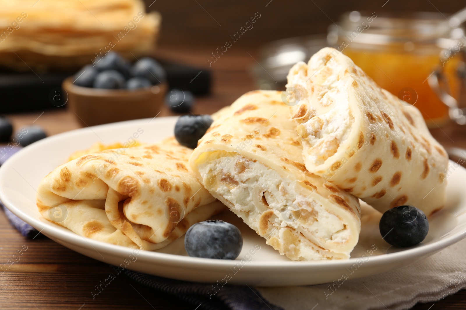 Photo of Delicious crepes with cottage cheese, jam and blueberries on wooden table, closeup