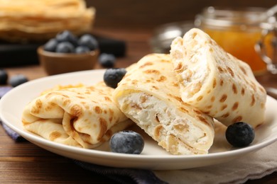 Photo of Delicious crepes with cottage cheese, jam and blueberries on wooden table, closeup