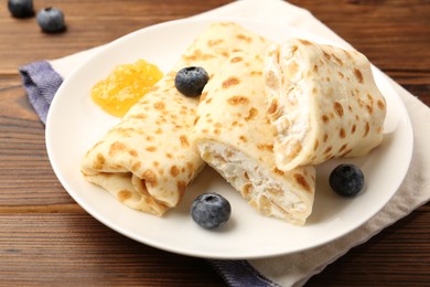 Photo of Delicious crepes with cottage cheese, jam and blueberries on wooden table, closeup