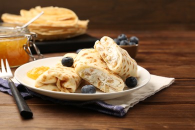 Photo of Delicious crepes with cottage cheese, jam and blueberries served on wooden table, closeup