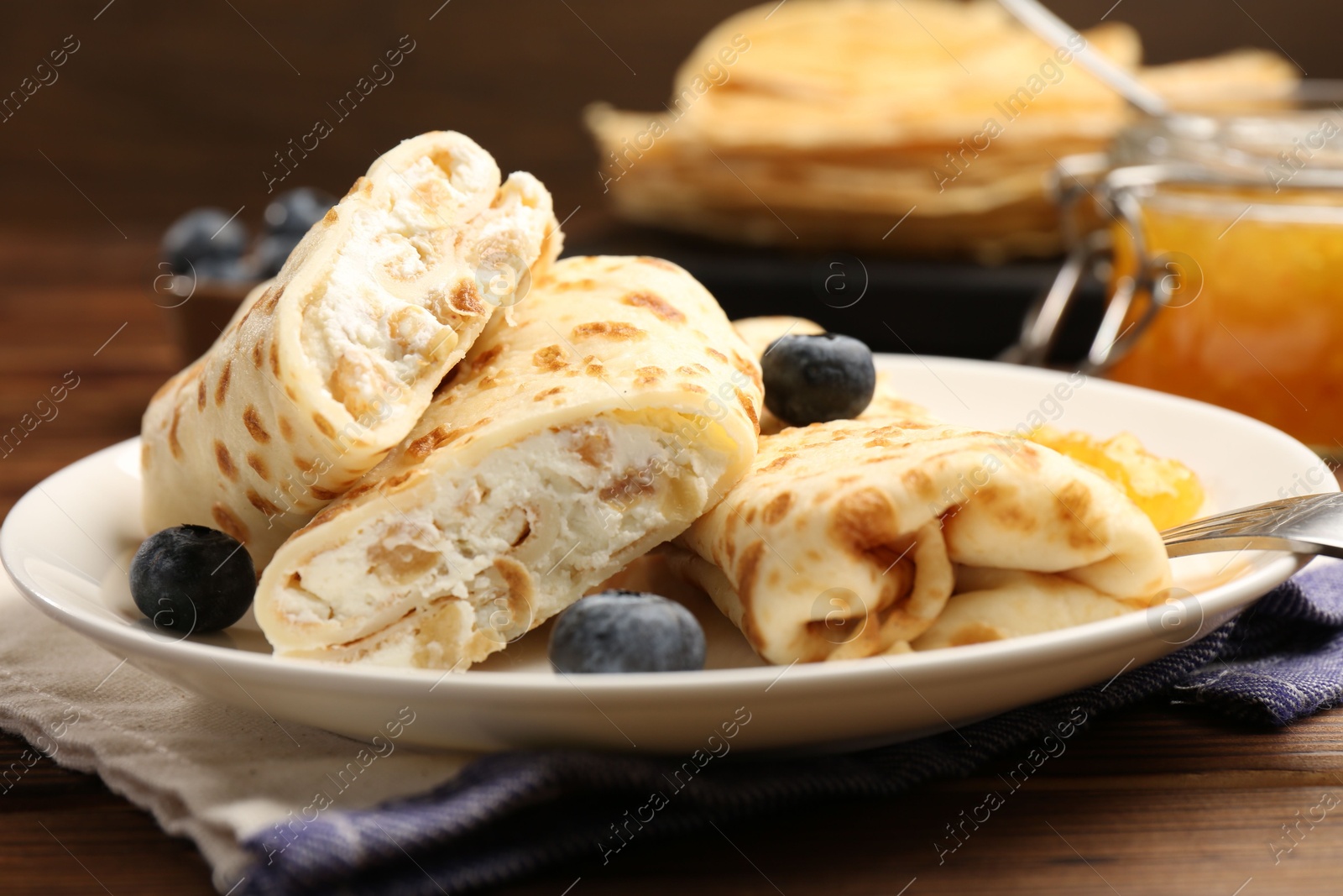 Photo of Delicious crepes with cottage cheese, jam and blueberries served on wooden table, closeup