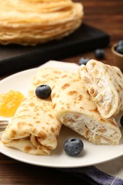 Photo of Delicious crepes with cottage cheese, jam and blueberries on wooden table, closeup