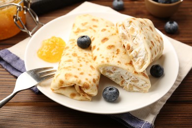 Photo of Delicious crepes with cottage cheese, jam and blueberries served on wooden table, closeup