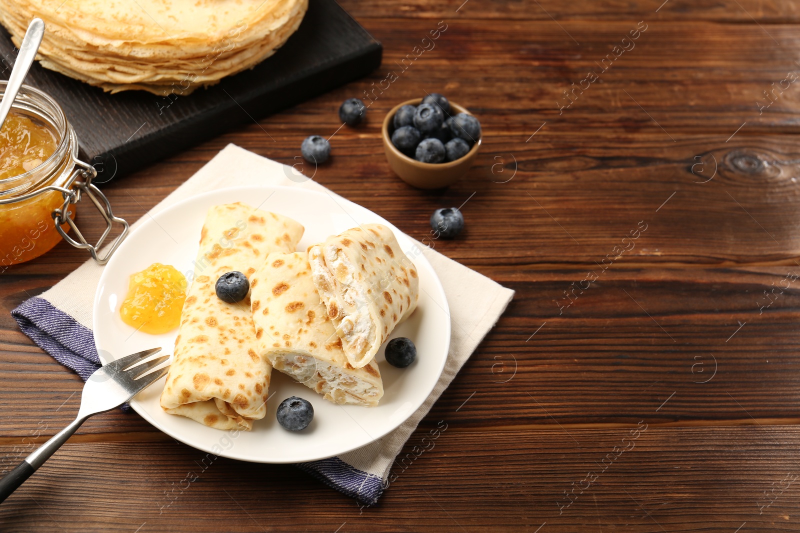 Photo of Delicious crepes with cottage cheese, jam and blueberries served on wooden table