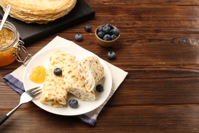 Photo of Delicious crepes with cottage cheese, jam and blueberries served on wooden table