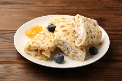 Photo of Delicious crepes with cottage cheese, jam and blueberries on wooden table, closeup