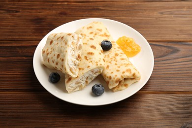 Photo of Delicious crepes with cottage cheese, jam and blueberries on wooden table, closeup