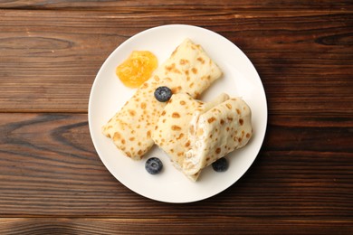 Delicious crepes with cottage cheese, jam and blueberries on wooden table, top view