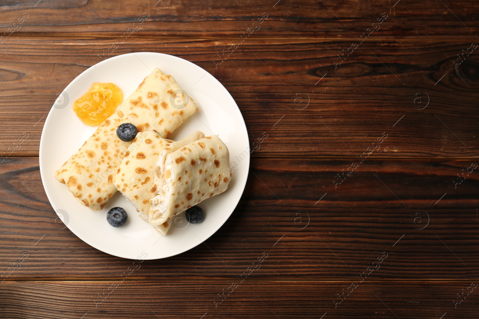 Photo of Delicious crepes with cottage cheese, jam and blueberries on wooden table, top view. Space for text