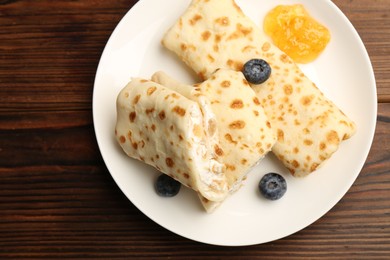 Delicious crepes with cottage cheese, jam and blueberries on wooden table, top view